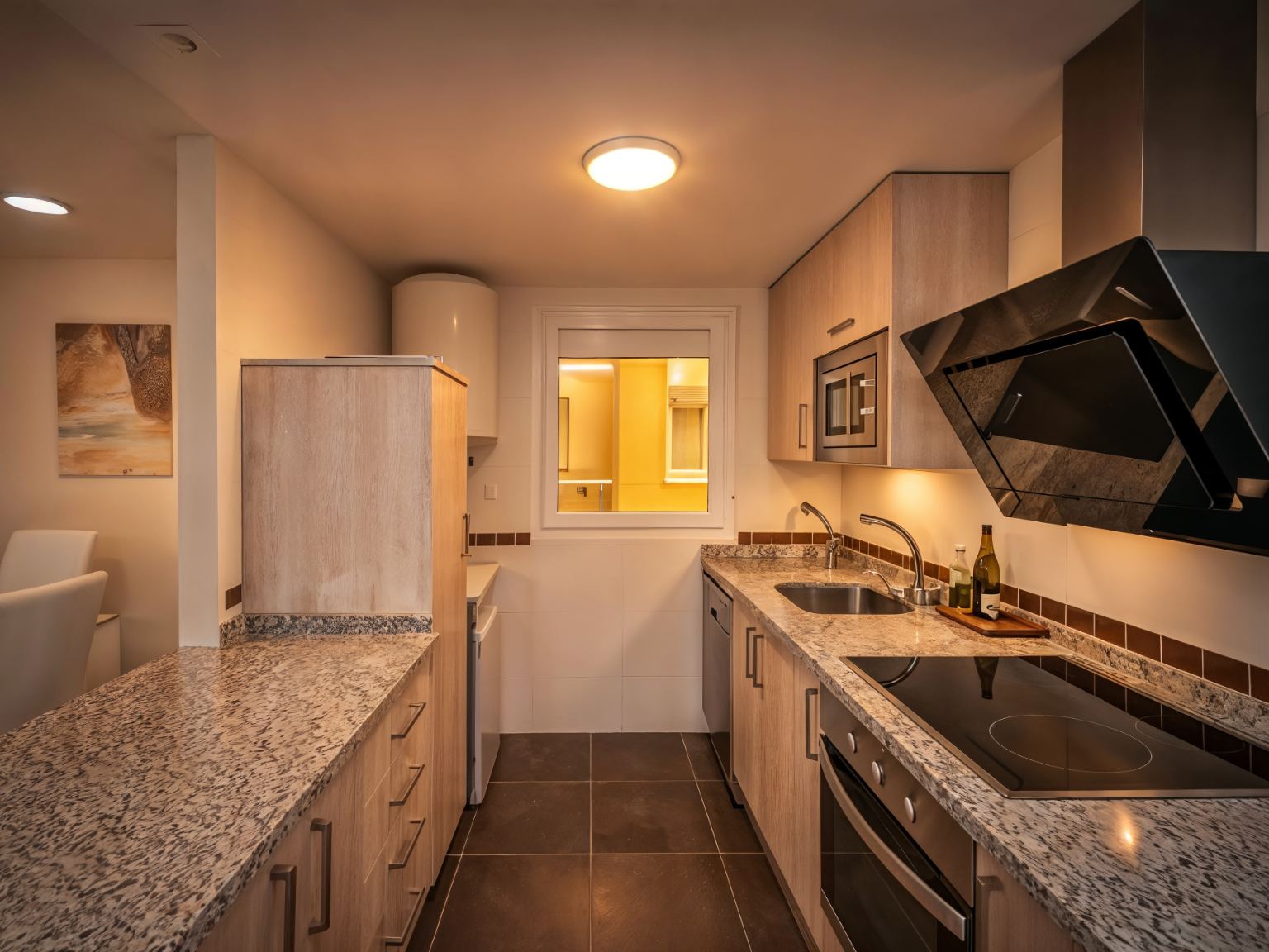 Cocina equipada de Nova MSuites Catedrales con armarios de madera clara, encimera de granito, vitrocerámica y horno